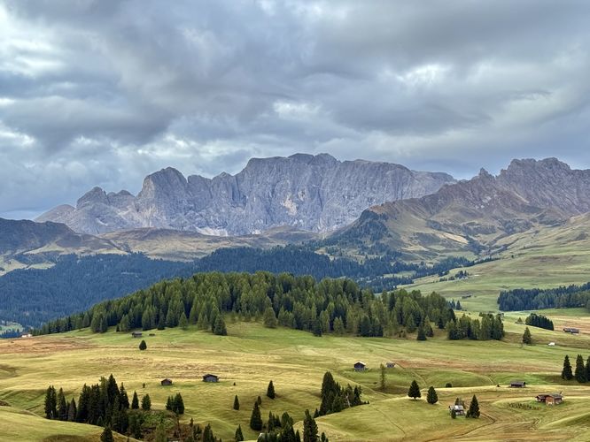 Rolling hill pastures with chalets dotting the landscape sit in the high-elevation meadows of Alpe di Siusi (Seiser Alm) with alpine ridges in the background