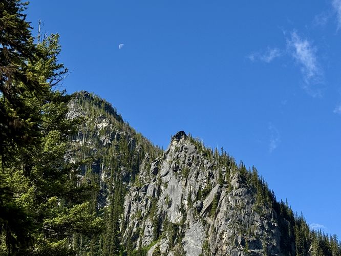 The moon sits in the sky above alpine peaks near Colchuck Lake