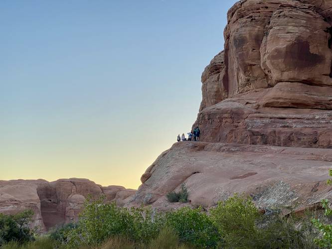 Hikers slowly make their way around the steep cliff area near Delicate Arch