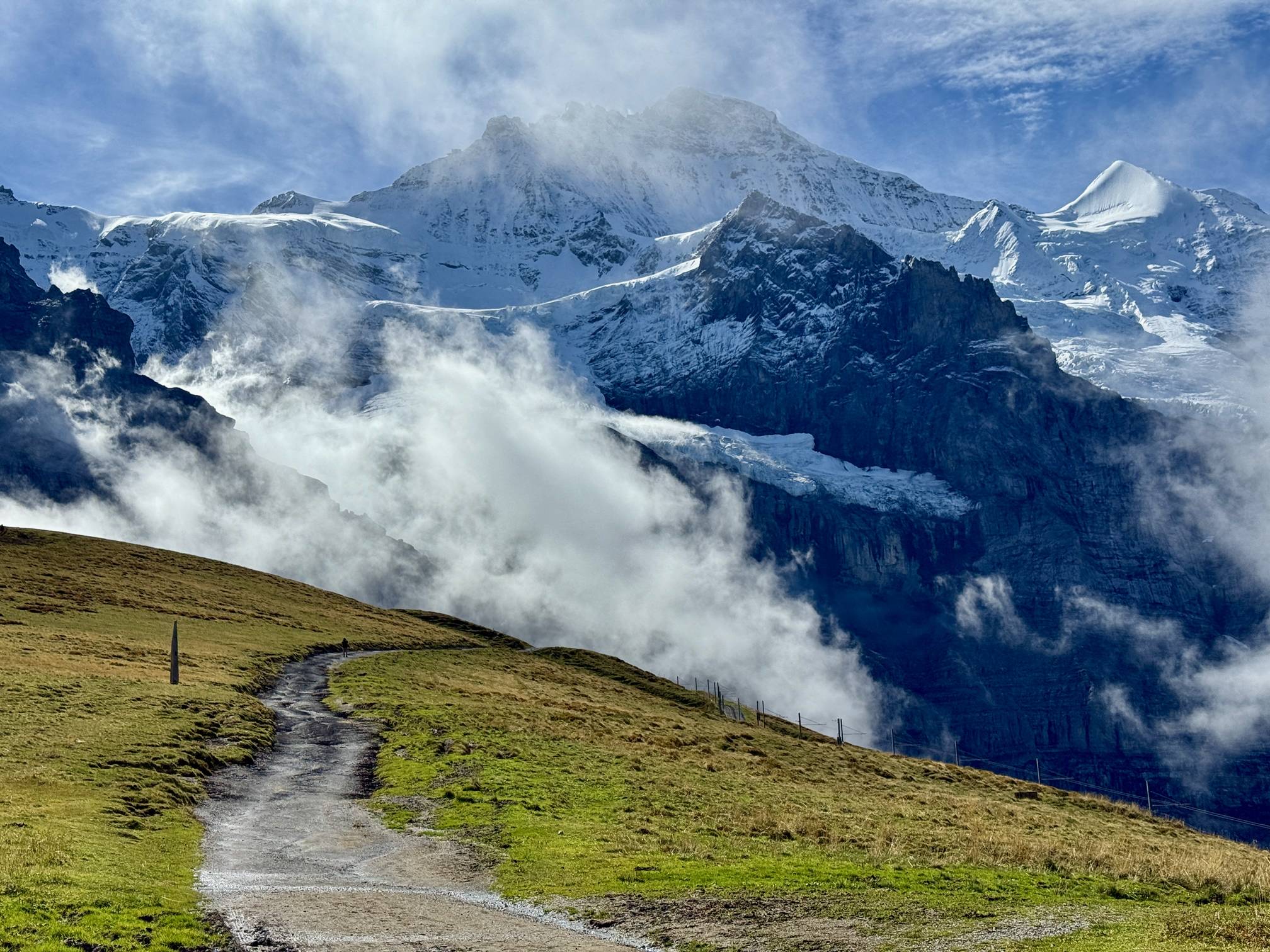 The towering alpine slopes of the Jungfrau stand over a winding trail in Grindelwald, Switzerland.