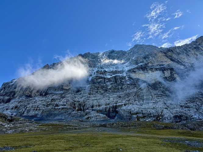 Clouds hover in front of the Eiger North Face illuminated by sunlight