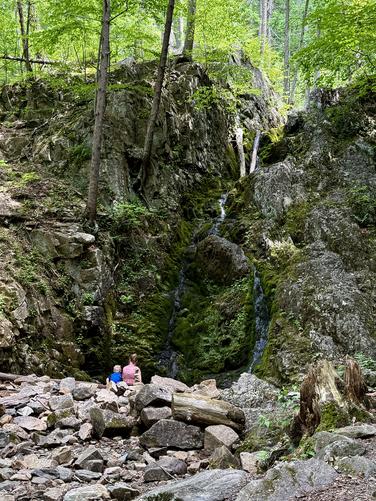 A hiker and small child sit below a trickling Fitzgerald Falls