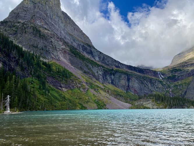 Hiker sits at Grinnell Lake with Angel Wing peak and Grinnell Falls overhead