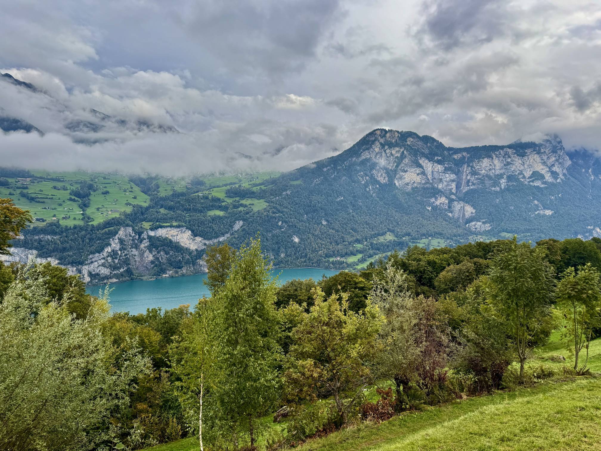A view of the turquoise waters of Walensee and the 585-meter tall Seerenbach Falls (Seerenbachfälle) with surrounding alpine mountains near Filzbach, Switzerland.