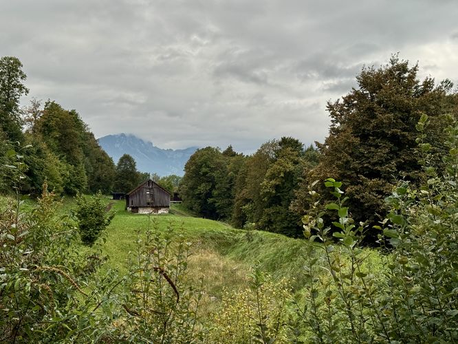 A barn sits in a meadow with mountain views in the distance