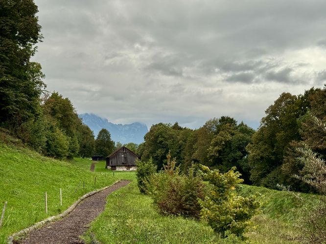 Another view of the Helsana Trail, a barn, and distant Swiss mountains