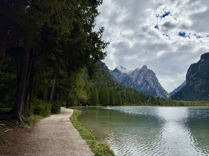 The flat trail of Lake Dobbiaco runs south along the edge of the water with views of towering alpine mountains