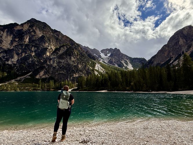 A hiker stands on the edge of Lago di Braies with alpine mountains of the Dolomites overhead