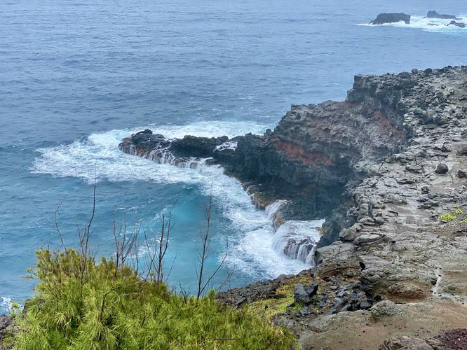 Seaside cliff waterfalls as ocean water retreats from the rock back to sea