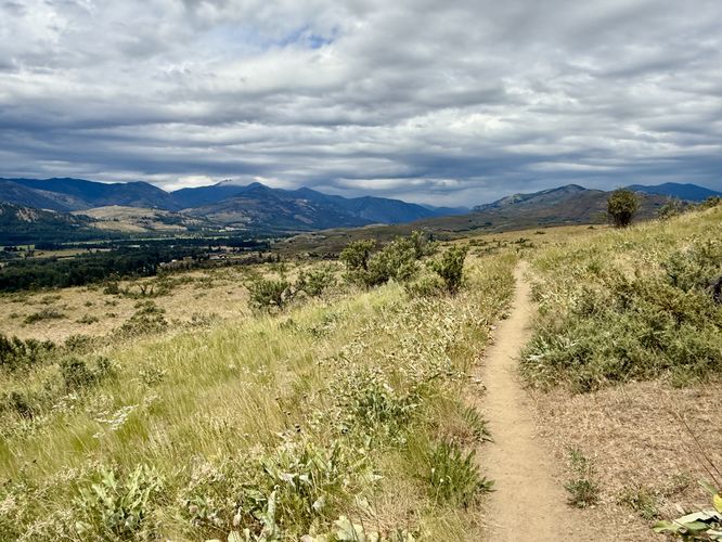 The Meadowlark Trail cuts through exposed grasslands with views of mountains in the distance