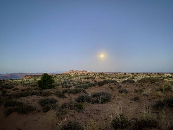 Moon sits above the desert on a sunrise hike to Mesa Arch