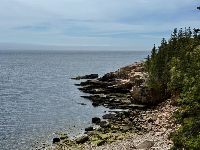 Hikers standing on the rocky coastline at Monument Cove