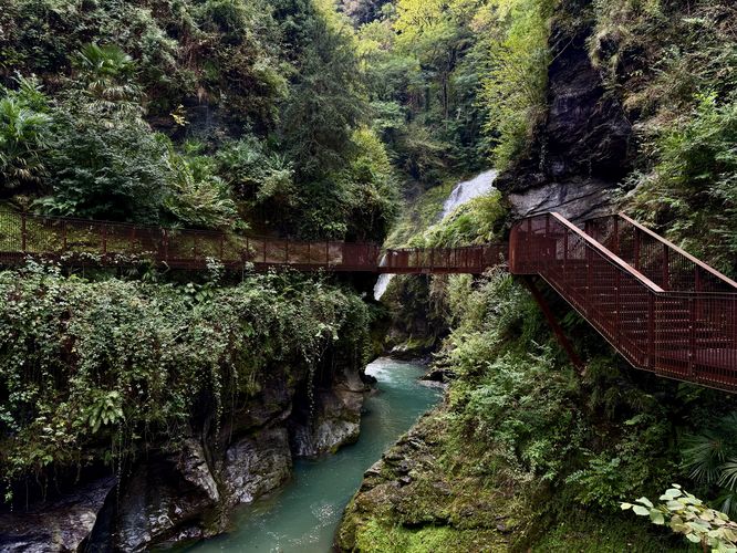 The gorge of Bellano (Orrido di Bellano) with a suspended trail that wraps through the canyon, turquoise pools of water, and a large waterfall in the background.
