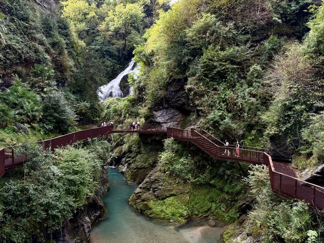 View of turquoise pools, a large waterfall, and the suspended bridges of Orrido di Bellano