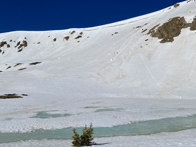 View of frozen Pass Lake and a slumping snow cliff - early June 2024