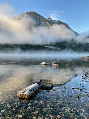 Colorful rocks in the lake with morning fog surrounding Red Eagle Mountain at Saint Mary Lake