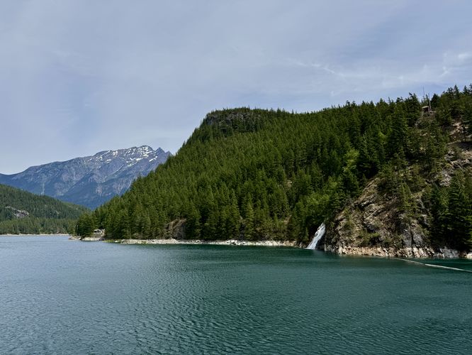 View of Lower Happy Creek Falls, turquoise waters of Ross Lake, and alpine mountains in the distance