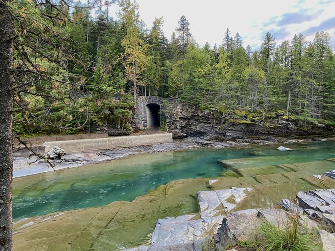 Deep turquoise pools within McDonald Creek with a stone tunnel across the water