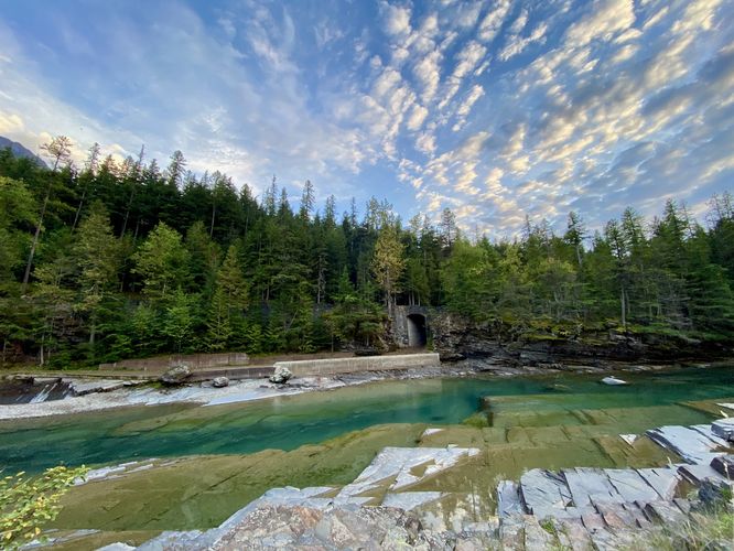 Deep turquoise pools within McDonald Creek with a stone tunnel across the water