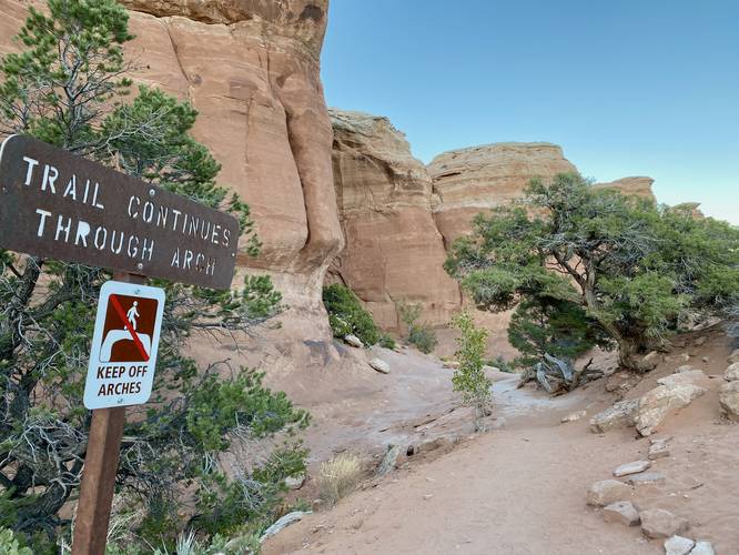 Sign reads "Trail continues through arch"