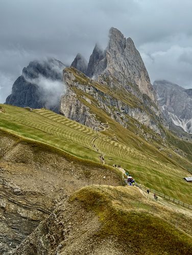 View of Seceda Ridge and its jagged alpine peaks. Below, hikers enter the pay-to-enter section of the trail 5 euro per person