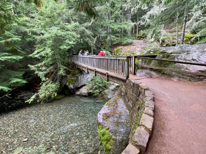 Bridge crosses Avalanche Creek with crystal-clear water and colorful rocks below